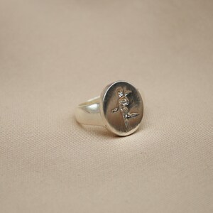 以下が含まれることがあります： 楕円形のトップにスタイリッシュな人物のレリーフデザインが施されたシルバーのシグネットリングです。