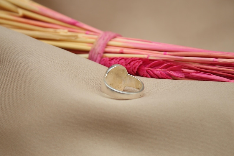 以下が含まれることがあります： 滑らかな楕円形のトップを持つシルバーリング。リングは薄い茶色の布地に置かれています。