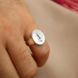 以下が含まれることがあります： 上面がスタイリッシュな葉のデザインで盛り上がっている銀の指輪。指輪は人の指にはめられています。