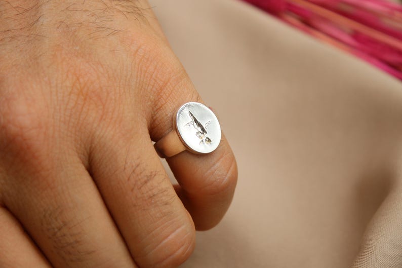 以下が含まれることがあります： 上面がスタイリッシュな葉のデザインで盛り上がっている銀の指輪。指輪は人の指にはめられています。