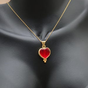 May include: A gold chain necklace with a red heart pendant. The heart is made of glass and has a gold border.