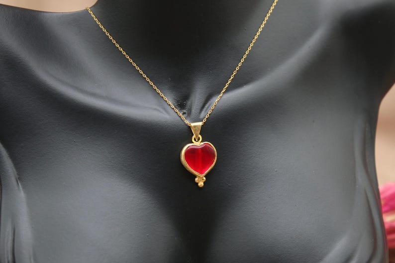 May include: A gold chain necklace with a red heart pendant. The heart is made of glass and has a gold border.