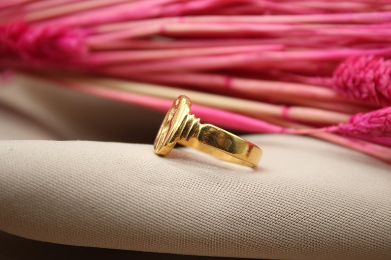 Op de afbeelding: Een gouden ring met een getextureerd ontwerp. De ring ligt op een beige stoffen achtergrond.