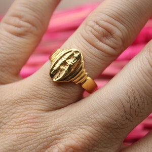 Op de afbeelding: Een gouden ring met een hartvormig ontwerp. De ring wordt aan een vinger gedragen.