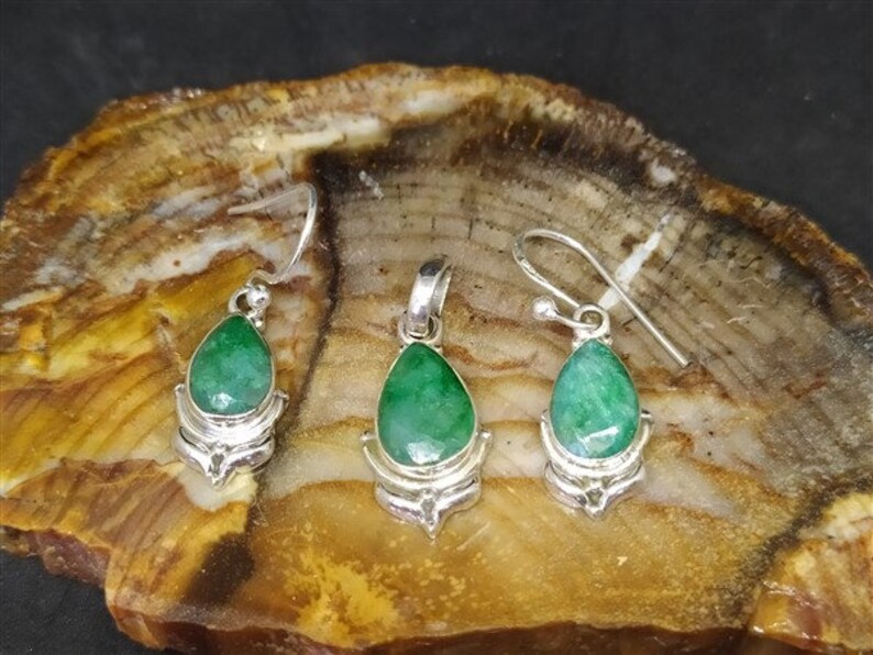 Pu&ograve; includere: Un set di gioielli con un ciondolo e due orecchini. Ogni pezzo ha una gemma verde a forma di goccia, incastonata in metallo color argento. Gli orecchini hanno chiusure a gancio e il ciondolo ha un anello per una catena.