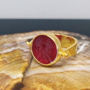 Peut inclure: Une bague en or avec une lunette ronde et rouge rotative orn&eacute;e d'un motif sculpt&eacute;. La bague est pos&eacute;e sur une surface en bois.