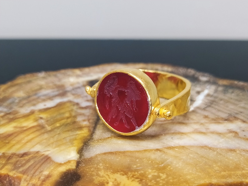 Peut inclure: Une bague en or avec une lunette ronde et rouge rotative orn&eacute;e d'un motif sculpt&eacute;. La bague est pos&eacute;e sur une surface en bois.
