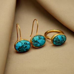 May include: A set of gold earrings and a ring with turquoise stones. The earrings are drop earrings with oval-shaped turquoise stones. The ring is a simple band with an oval-shaped turquoise stone.