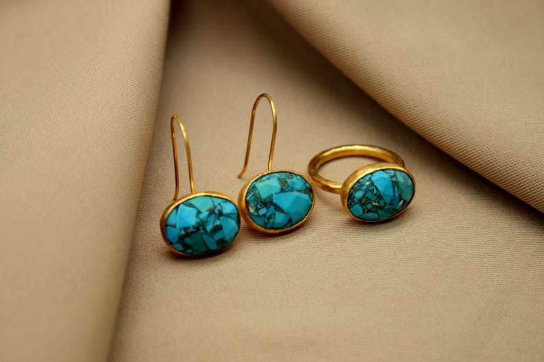 May include: A set of gold earrings and a ring with turquoise stones. The earrings are drop earrings with oval-shaped turquoise stones. The ring is a simple band with an oval-shaped turquoise stone.