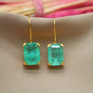 Puede incluir: Un par de pendientes de oro con gotas de piedras preciosas verde esmeralda. Los pendientes tienen un diseño sencillo y son perfectos para el uso diario.