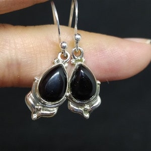 May include: A pair of silver dangle earrings with black teardrop-shaped stones. The stones are set in a silver frame with a decorative design.