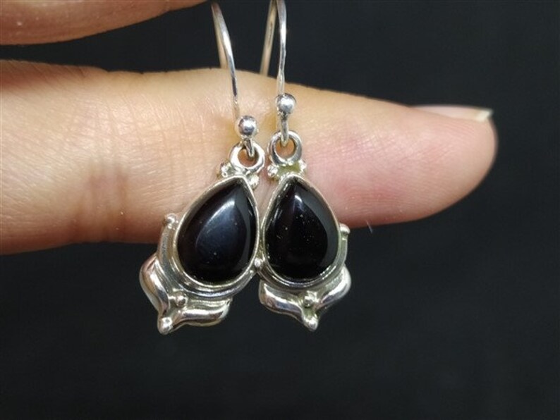 May include: A pair of silver dangle earrings with black teardrop-shaped stones. The stones are set in a silver frame with a decorative design.