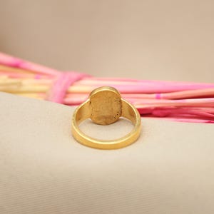 May include: A gold ring with a smooth oval-shaped stone set in the center. The ring is shown from the back, revealing the smooth gold band.