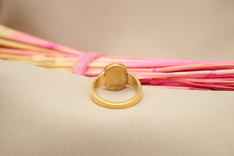 May include: A gold ring with a smooth oval-shaped stone set in the center. The ring is shown from the back, revealing the smooth gold band.
