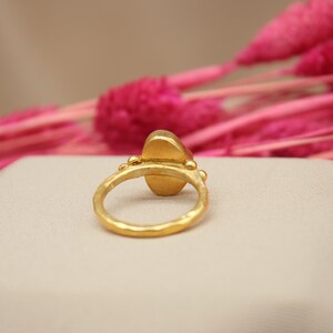 May include: A gold ring with a large oval-shaped gemstone. The ring is set with small gold beads around the gemstone.