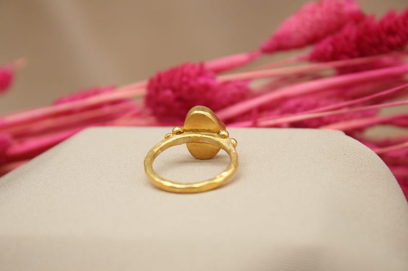 May include: A gold ring with a large oval-shaped gemstone. The ring is set with small gold beads around the gemstone.