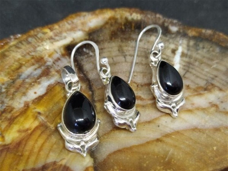May include: A set of silver earrings and a pendant featuring black gemstone drops. The earrings are teardrop shaped with a delicate floral design. The pendant is similar in style, with a slightly larger gemstone.
