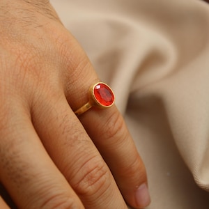 May include: A gold ring with a large, oval-shaped, red gemstone.