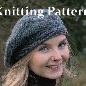 May include: A woman wearing a blue and green knitted beret with a small black nose ring. The beret has a subtle marled effect and a small tag on the side.