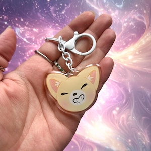 Könnte beinhalten: Ein Schlüsselanhänger mit einem Cartoon-Shiba-Inu-Hund mit einem glücklichen Ausdruck. Der Schlüsselanhänger ist aus klarem Acryl und hat eine silberne Metallkette und einen Karabiner.