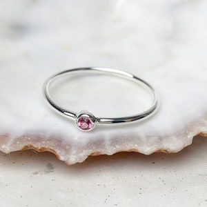 Könnte beinhalten: Ein zarter Silberring mit einem kleinen rosafarbenen Edelstein in der Mitte.