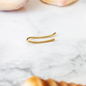 Op de afbeelding: Een gouden haarspeld op een wit marmeren oppervlak met schelpen eromheen.