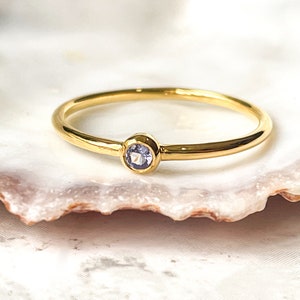 May include: A delicate gold ring with a small, round, light blue gemstone.