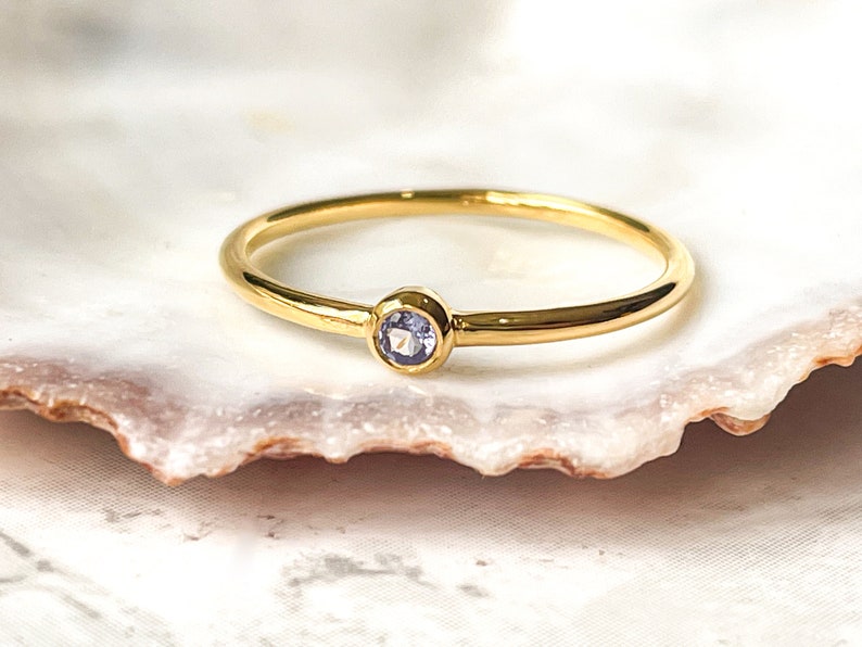 May include: A delicate gold ring with a small, round, light blue gemstone.