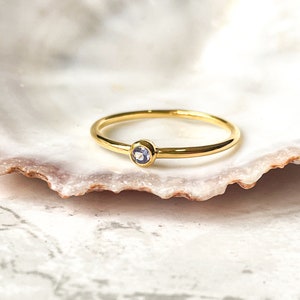 May include: A simple gold band ring with a small, light purple gemstone set in the center.