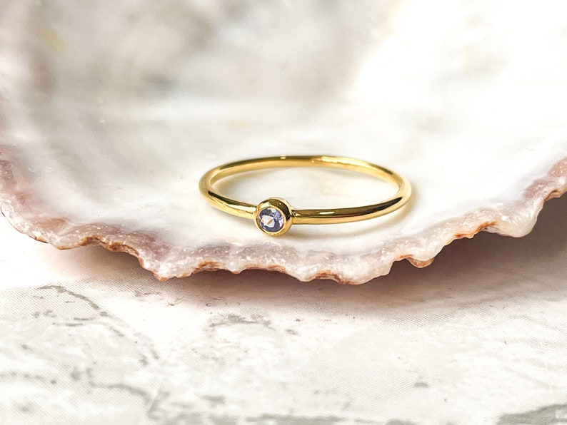 May include: A simple gold band ring with a small, light purple gemstone set in the center.