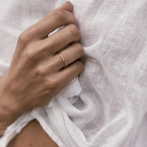 May include: A delicate gold ring with a small black gemstone. The ring is worn on the finger of a person's hand.