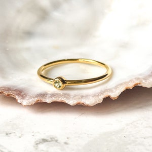 May include: A simple gold ring with a small, light green gemstone set in the center.