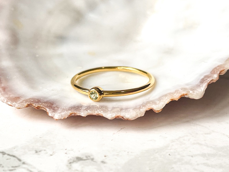 May include: A simple gold ring with a small, light green gemstone set in the center.