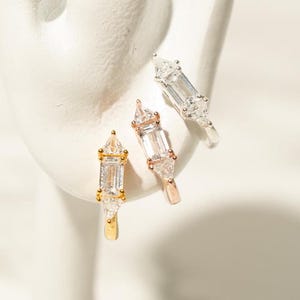 Könnte beinhalten: Drei Creolen in Gold, Silber und Roségold mit einem rechteckigen und dreieckigen Design aus klarem Kristall.