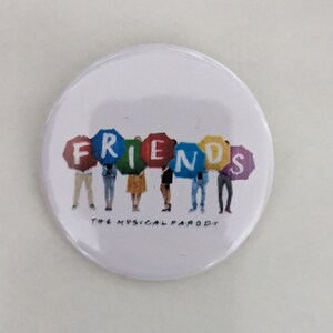 Puede incluir: Un botón blanco con una imagen colorida de seis personas sosteniendo carteles que deletrean "FRIENDS" en colores arcoíris. El texto "THE MUSICAL PARODY" está impreso debajo de la imagen.