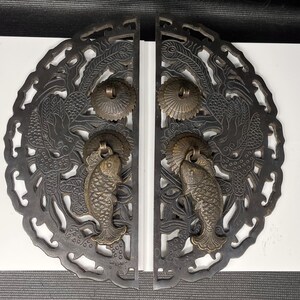May include: A pair of dark metal semi-circular door plates featuring intricate openwork carvings of birds and floral patterns. Each plate includes a circular brass-toned mount and a hanging fish-shaped door knocker with textured scale details.