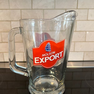 May include: A clear glass pitcher with a red and white logo that says "Molson Export".
