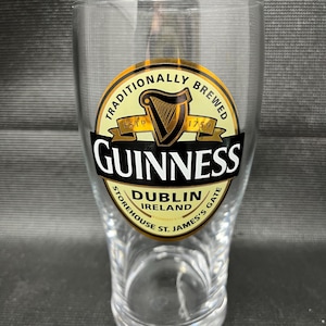 May include: A clear pint glass with the Guinness logo. The logo features a harp, the word "Guinness" in bold black letters, and the words "Dublin Ireland" and "Traditionally Brewed".