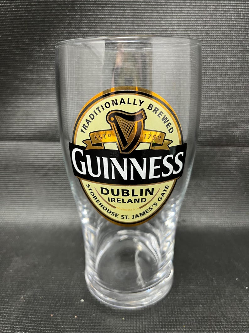 May include: A clear pint glass with the Guinness logo. The logo features a harp, the word "Guinness" in bold black letters, and the words "Dublin Ireland" and "Traditionally Brewed".