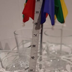 May include: A colourful rainbow umbrella with a metal stand, measuring 13 inches in length, is placed in a white wire rack with clear glass cups.