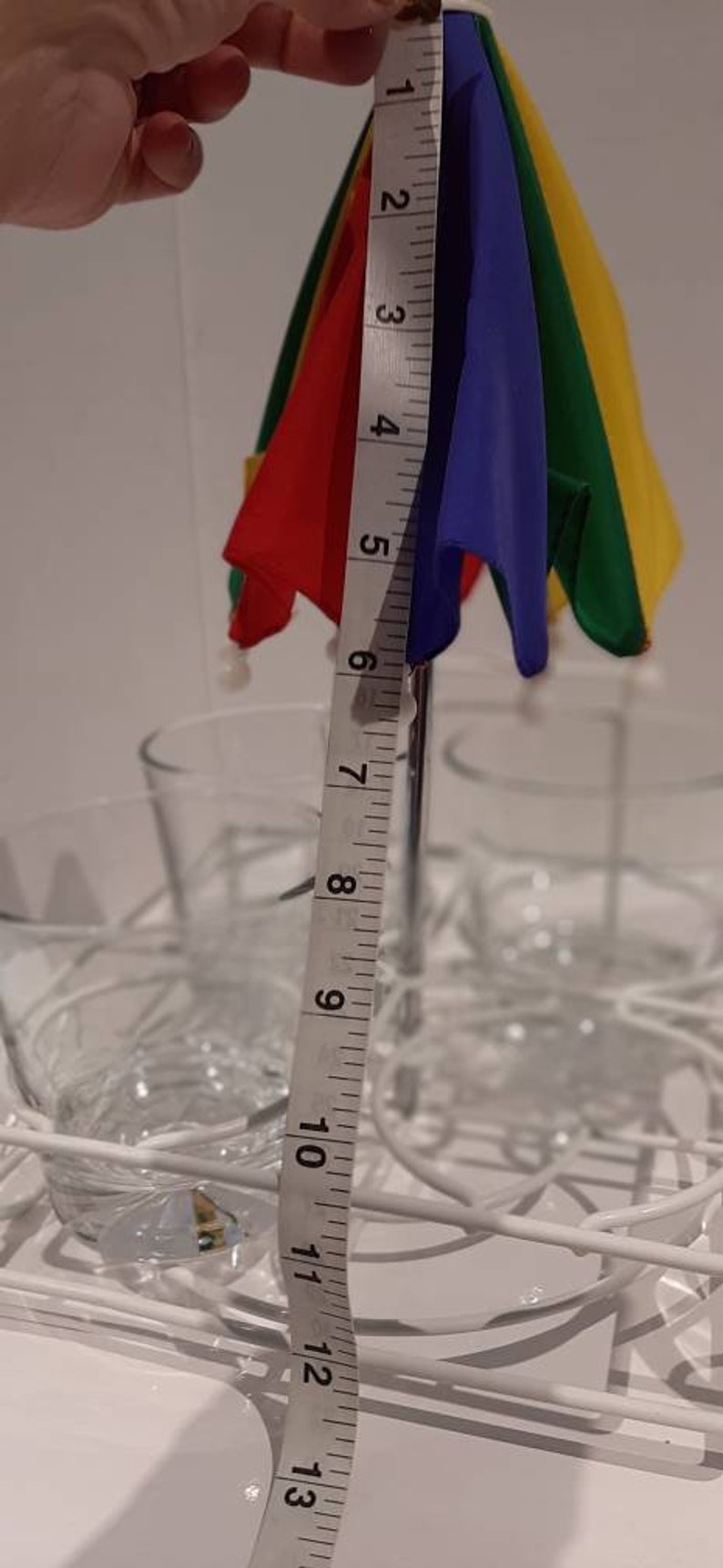 May include: A colourful rainbow umbrella with a metal stand, measuring 13 inches in length, is placed in a white wire rack with clear glass cups.