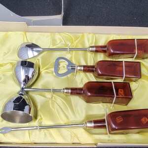 May include: A set of five silver cocktail tools in a yellow velvet-lined box. The set includes a jigger, a bottle opener, a spoon, and two small bottles with dice inside.