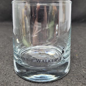 May include: A clear glass tumbler with the words "JOHNNIE WALKER" printed on the bottom.