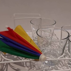 May include: A white metal dish rack with five clear glass cups. A colourful, multi-striped umbrella is resting on the rack.