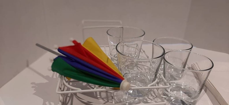 May include: A white metal dish rack with five clear glass cups. A colourful, multi-striped umbrella is resting on the rack.