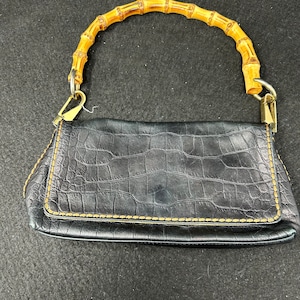 May include: A black leather handbag with a bamboo handle. The bag has a crocodile-embossed texture and gold-tone hardware.