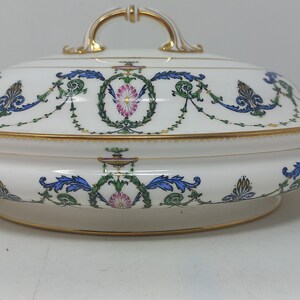 May include: White oval serving dish with a lid, featuring a floral design in shades of blue, green, pink, and gold. The dish has two handles and a gold rim.