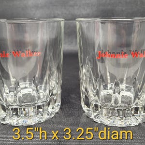 May include: Two clear, faceted whiskey glasses with the red "Johnnie Walker" logo. Each glass is 3.5 inches high and 3.25 inches in diameter. The glasses have a decorative, textured base.