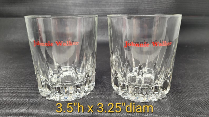 May include: Two clear, faceted whiskey glasses with the red "Johnnie Walker" logo. Each glass is 3.5 inches high and 3.25 inches in diameter. The glasses have a decorative, textured base.