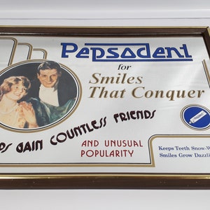 Pode incluir: Um espelho publicitário vintage para a pasta de dentes Pepsodent. O anúncio apresenta um casal sorrindo e o texto "Pepsodent para sorrisos que conquistam inúmeros amigos e uma popularidade incomum. Mantém os dentes brancos como a neve, os sorrisos ficam deslumbrantes."